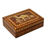 Caixa para joias marroquina em madeira nobre. Formato retangular com decoração de marqueterie de madeiras claras Tampa com reserva apresentando figuras de dromedários. Interior forrado com veludo vermelho. 4,5 x 15 x 10,5 cm. Pertenceu ao Espólio de Vitória Dib Bachour.