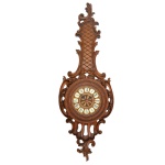 Relógio de parede, funcionando. Caixa em madeira entalhada e decorada com volutas w vazados. Mostrador em algarismo romano. Marca .......... 95 x 33 cm. Pertenceu ao Espólio de Vitória Dib Bachour.