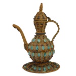 Bule marroquino com bandeja em metal amarelo, decorada com esmalte policromático com aplicações de pedraria. Apresenta decoração predominante de dourado e azul. Bandeja circular de mesma decoração. Séc. XX. (26 cm) com pires (15 cm). Pertenceu ao Espólio de Vitória Dib Bachour.