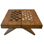 Tabuleiro marroquino para jogos com decoração em marqueterie de madeiras claras e madrepérola. Tabuleiro dobrável e de formato retangular. Base de madeira no mesmo estilo e dobrável. Interior seguindo a mesma decoração. Acompanha pedras para jogo de dama. Pertenceu ao Espólio de Vitória Dib Bachour.