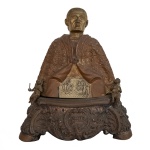 Rara escultura maçônica europeia em bronze com várias pátinas, representando provavelmente um Grão-mestre de uma das Ordens, ladeado por pequenas figuras de Putti. Apresenta-se sentado sobre base cônica decorada com folhagens e volutas centralizando adornos simbólicos em reserva. Traz vestes cerimoniais realçadas por rica capa bordada, exibindo à frente placa com cena de decapitação de um bispo, possivelmente o próprio, em presença do rei. Verso da imagem apresentando medalhão com símbolos da maçonaria. Peça de coleção de importante simbologia. Séc. XIX. 34 cm x 30 cm . Circa de 1800. Falta uma pedra.