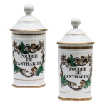 Par de potes de farmácia em porcelana da manufatura francesa. Superfície branca apresentando rótulos com as inscrições Poudre de Cantharide e Poudre de Cantharide. França. Séc. XX. 27 cm.