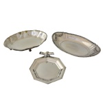 Conjunto de três peças em metal prateado, constando de: A) Cesta de forma oval com borda com godrões e guirlandas (4 x 26 x 17 cm); B) Cesta de forma oval e recortada com pezinhos (4 x 22 x 15 cm); C) Covilhete octogonal com decoração na forma de nó (16 cm). Sinais de uso.