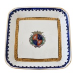 Covilhete de porcelana portuguesa, de forma quadrada. Borda com friso azul e faixa em ouro na parte de dentro da peça. Centro com brasão. Séc. XX.  15 x 15 cm.