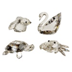 SWAROVSKI - Conjunto de quatro peças em cristal austríaco translúcido e lapidado Borda encimada por dois pássaros. Constando de cisne, coelho, siri e tartaruga. 3 cm maior / 2 cm menor. Swarovski é o nome do cristal mais conhecido no mundo da moda por sua delicadeza, precisão e brilho. A companhia austríaca Swarovski AG, foi fundada por Daniel Swarovski que inventou uma máquina de corte automática em 1892.  Desde a sua fundação até os dias atuais, a marca foi fazendo fama na medida em que os cristais Swarovski foram se popularizando.