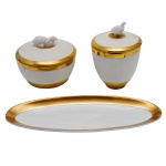 Conjunto de peças de porcelana portuguesa, com decoração similares, superfície branca com frisos em ouro. Sendo: dois potes com velas comemorativas e tampa na forma de coelho e galinhas. Marcado no fundo: Palácio de Mafra. Instituto dos Museus e Conservação, Portugal.  (9 x 11 cm / 13 x 9 cm) e covilhete de forma oval. No fundo marcado Vista Alegre. 13 x 8 cm.