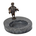Cinzeiro em mármore encimado por estatueta de menino segurando dois porcos.  9 cm. Base 2 x 17 cm.