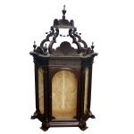 Oratório de mesa em madeira nobre, de formato chanfrado com frente e laterais envidraçadas. Parte superior construída com adornos no formato de conchas e pequenas urnas com cruzes, encimada por braços recortados sustentando arremate com idênticos adornos. Pés largos e curtos. Possivelmente do século XIX. 183 x 109 x 44 cm.