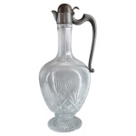 Jarra francesa para vinho em cristal com montagem em metal branco. Bojo no formato de balaústre, lapidado e ornado com treliças e feixes apoiado em base circular. Alça em S e bico curto. Peça provavelmente de titular brasileiro. Marca da Cristallerie Baccarat no metal. 26 cm.