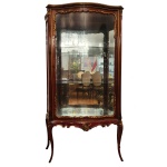 Vitrine estilo francês em madeira nobre decorada por frisos dourados. Caixa retangular abaulada com uma porta à frente, laterais envidraçadas apresentando prateiras na parte interna. Pernas levemente arqueadas. 150 x 88 x 43 cm.