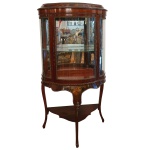 Vitrine de pé estilo francês Louis XV, ornamentada por frisos estilizados, de formato retangular com frente em meia lua. Armário com laterais e porta envidraçadas, encimado por frontão liso e bordas salientes. Parte inferior com saia ondulada realçada em marqueterie por cena com putti. Pernas recurvas reunidas à meia altura por pequeno plateau. 147 x 75 x 36 cm. R$5.000,00