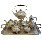 Excepcional conjunto para chá e café em metal francês, espessurado a prata. Corpo robusto de dimensão circular inteiramente guilhochado, envolvendo reserva alisada e moldurada com escudo, rematado a cinzel com representações vegetais. Bico curvo e alça recurva em Pega da tampa representando botão de flor sobre folhas esparramadas. Isoladores de marfim. França. Séc. XIX. Constando de seis peças, sendo: grande bandeja com alças (73 x 50 cm); samovar (38 x 29 cm); bule p/ café (23 x 21 cm); bule p/ chá (15 x 18 cm); açucareiro (13 x 20 cm); cremeira (12 x 18 cm),