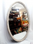 Espelho oval bisotado com moldura em madeira entalhada com patina branca. Medindo 90cm x 60cm.