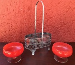 Suporte para galheteiros em metal prateiado com cinzelado vazado, acompanham duas taças em vidro, com coloração avermelhada. Altura 26cm, Diâmetro das taças, 9cm.