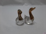 Par de enfeites na forma de cisne em vidro com cabeça e pescoço em metal dourado. Medindo 11,5cm de altura.