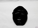 Máscara em madeira escura para pendurar. Medindo 21,5cm x 14cm.