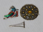 BIJUTERIA - Três broches: a) Dois pássaros em esmalte. 4 x 6cm. b) Torre Eiffel estilizada. 5 x 2cm c) Oval, metal prateado decorado com flores e pedras âmbar. 6 x 5cm. Todos com leves sinais de uso.