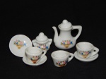 Miniatura de conjunto para chá em porcelana branca aplicada com desenhos de flores, composto por: bule, açucareiro, 3 xícaras e 3 pires. Um dos pires com bicado. Alt. bule 4cm.