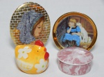 Quatro peças diversas em porcelana: a) Placa oval aplicada com pintura feminina à mão, fundo em dourado. 10,5 x 8cm. b) Porta-copos colecionável aplicado com transfer-printing de menina com cachorro. Coleção Nostalgic Childhood. Diâm. 9cm. c) Pequeno saleiro na forma de galinha policromada. Apresenta fio de cabelo. Alt. 5cm. d) Caixinha decorada com rosa rajado. Marcada Schmidt. 2,5 x 8cm.