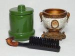 Três peças diversas: a) Escova para sapatos em plástico rígido, cabo ornamentado com cabeça de cavalo policromada esmaltada em resina. Comp. 18cm. b) Pequeno cálice decorativo em resina policromada, ricamente ornamentado com folhagens e volutas, aplicado com camafeu no centro. Alt. 10 x 9 x 11cm. c) Pote em cerâmica vitrificada verde. Alt. 11cm.