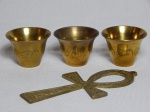 Quatro peças em metal dourado: cruz Ansata e 3 copinhos com folhagens cinzeladas. 13 x 7cm e 3 x 5cm.