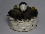 Caixa porta-joias em cerâmica vitrificada branca, tampa ornamentada com cabeça de pierrot, aplicada com tecido em babado. Selo da Companhia da Terra. 13 x 15cm.