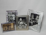 Quatro porta-retratos diversos: 2 com molduras em placas de prata, 1 em resina prateada e 1 aplicado com pedrinhas plásticas. Maior 21 x 16cm, menos 14 x 9,5cm.