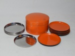 Dois conjuntos de porta-copos: caixa contendo 6 em baquelite laranja, e 7 porta-copos soltos em metal aplicado no centro com monograma UB. 6 x 9cm e diâm 8cm.