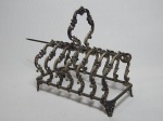Porta-torradas em metal ornamentado com volutas e folhagens moldadas. Marcas do tempo. 17 x 17 x 9cm.