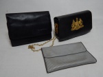 Lote com 3 bolsas: a) Necessaire em couro da companhia aérea Lufthansa, contendo kit com pente, sabão, protetor auricular, removedor de pelos, lixa e máscara de dormir. 15 x 20 x 6cm. b) De mão, em couro rígido, brasão com lema do Reino Unido em metal. 13 x 20 x 6cm. Marcas do tempo. c) Carteira de mão em tecido revestido por plástico. Marcada Jal. 13 x 19cm.