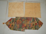 Três peças em tecido: a) Par de capas para almofada, revestida por tecido em palha de milho trançado, 49 x 49cm. b) Caminho de mesa policromado com cenas campestres. 84 x 30cm.