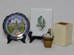 Quatro peças decorativas diversas em porcelana: a) Casa de bosque em pasta de porcelana policromada. 11 x 12 x 9cm. b) Caixinha na forma de balde com champagne. Alt. 8cm. c) Pratinho alemão com desenho de Palácio de Karlsruhe. Diâm. 11cm. d) Placa com ramos de alecrim pintados à mão. 12 x 10cm.