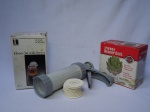 Três utensílios de cozinha: a) Bomba para modelagem de biscoitos, confeccionada em plástico, patente da Wilton. Acompanha formas para diversos formatos. Comp. 22cm. b) Pote em acrílico para serviço de mel. Na caixa original. Alt. 14cm. c) Suporte para cozinhar alcachofras em inox. Na caixa original. Apresenta desgastes. 7 x 11cm.