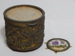 Caixa de música, fundo em madeira, parte externa em metal amarelo moldado com laços e florais, tampa aplicada com placa de porcelana francesa Limoges soltando. Funcionando. Marcas do tempo. 8 x 8cm.