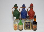 Sete garrafas de bebidas em miniatura: a) Três garrafas revestidas por palha trançada vermelha, verde e azul. Alt. 16cm. b) Quatro colecionáveis: 