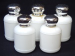 Cinco frascos vazios do perfume Anais Anais, da Cacharel, confeccionados em vidro leitoso branco, tampa em metal. Alts. 12 e 10cm.
