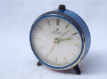 JUNGHANS - Relógio despertador de mesa em metal amarelo com placa esmaltada em azul, mostrador com marcadores em barras, modelos Bivox-silentic. Marcas do tempo e desgastes, necessita reparo. 7 x 7 x 3cm