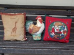 Três almofadas diversas: uma na forma de galo, uma com decoração natalina de Papai Noel e uma com bordagem de girafa. 39 x 30cm, 41 x 41cm e 46 x 46cm.