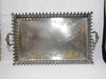 Grande tabuleiro em metal espessurado a prata, centro cinzelado com volutas e folhagens, galerias vazadas com penas, pés e alças moldadas com folhagens. Marcas do tempo. 65 x12 x 47cm.