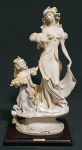 GIUSEPPE ARMANI. Belíssima escultura de resina italiana representando mulher e criança, sobre pedestal de madeira. Peça assinada. Mede 37 cm de altura. Excelente estado