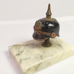 MILITARIA - Miniatura de Capacete de ponta (Pickelhaube) do Exército Chileno, fixado em base de marmore. A base mede 10,5 X 07 cm. Uma ponta da base está danificada.