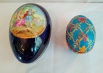 Um porta joias em porcelana, em formato de ovo, com figura de sena galante, medindo 15x10cm e 10cm de altura, e outro em madeira, formato de ovo, com decoração de flores e laços.