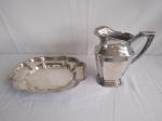 Duas peças em metal, sendo uma jarra para água, marca Meridional, medindo a boca 13x9cm e 21cm de altura, e uma pãozeira, medindo 30x22cm.