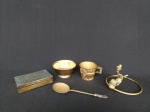 Cinco itens em metal dourado, sendo um porta toalha, em formato de argola adornado com peixe, uma caixa, uma caneca, um bowl e uma colher.