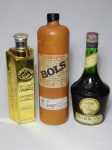 Três garrafas especiais de bebidas antigas: a) BOLS - Garrafa em cerâmica da tradicional bebida holandesa jevener, produzida pela distilaria BOLS, 1 litro. Início do século XXI. Alt. 31cm. b) Em vidro dourado do licor de chocolate suiço Goldkenn. Vazia. Alt. 25cm. c) Antiga do licor Bénédictine, fabricado pela distilaria D.O.M., 750ml. Possivelmente impróprio para consumo. Alt. 26cm.