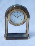 Relógio de mesa à bateria, estrutura em bronze, mostrador com marcadores em algarismos romanos, marcado NATAN. Desgastes e marcas do tempo, necessita reparos. 14 x 10 x 3cm.