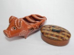 Duas peças em cerâmica vitrificada: a) Pote oval em tons marrons, tampa com decoração em xadrez, pega da tampa na forma de pato. 6 x 17 x 13cm. b) Floreira marrom na forma de porco decorada co folhagens pintadas à mão. 12 x 28 x 11cm.