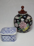 Duas peças em porcelana: a) Potiche chinês, decoração de flores e folhagens sobre fundo preto, tampa adaptada em madeira. Marcado no fundo. Alt. 16cm. b) Caixinha em fundo branco, decoração em azul. 5 x 8 x 8cm.