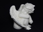 Figura de anjo confeccionada em pasta de porcelana patinada de branco. Pequeno fio de cabelo na asa e mancha na pátina na região da sobrancelha. Bicado no cabelo. 25 x 23 x 23cm.