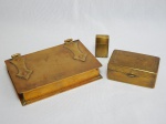 Três peças em metal amarelo: a) Caixa possivelmente cigarreira, tampa cinzelada com nome não identificado, datada de 28/9/1922. 4 x 9 x 5cm. b) Caixa porta-charutos moldada na forma de livro. Alguns amassados. 3 x 16 x 10cm. c) Porta-lâminas, marca da Gillette na tampa. 5 x 3 x 1cm.